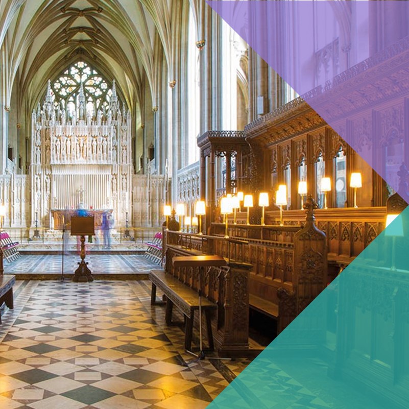 The aisle of a church facing the altar. On either side, wooden structures where the choir stands are lit with several lamps.